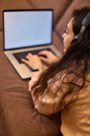 Caucasian woman in headphones using laptop and lying on sofa at homeの写真素材