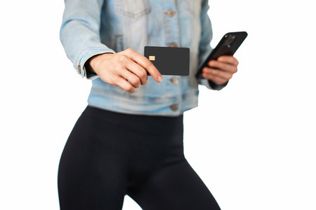 woman in denim holding mobile phone and credit card on white background. woman paying with plastic credit card on smartphone app,の写真素材