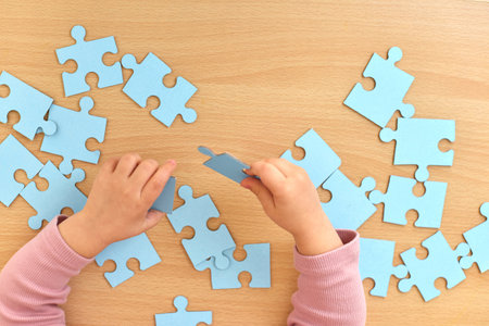 hands of little child arranging blue puzzle on wooden desk, top view, Education concept.の写真素材