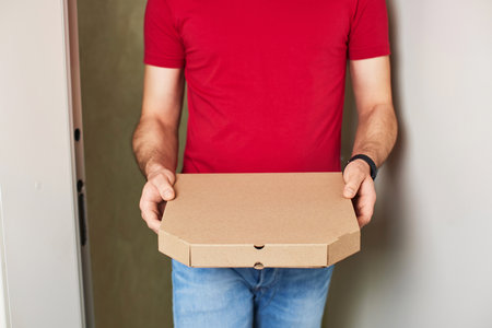 delivery man giving food order and holding pizza box standing at doorwayの写真素材