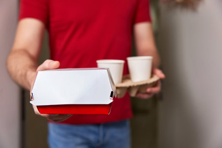 delivery man giving food box and paper coffee cups to customer at his front doorの写真素材