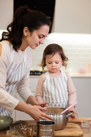 mother and her little child daughter in aprons preparing the dough in the kitchen, bake cookiesの写真素材
