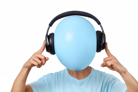 woman hides her face behind balloon with headphones on white backgroundの写真素材