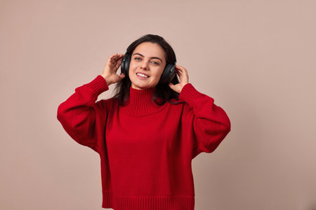 Happy girl wearing red sweater and headphones enjoying listening music on pink background.の写真素材