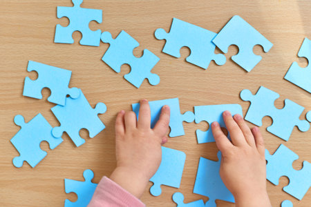 hands of little child arranging blue puzzle on wooden desk, top view, Children development.の写真素材