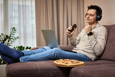 freelancer man using smart phone and laptop on sofa at homeの写真素材
