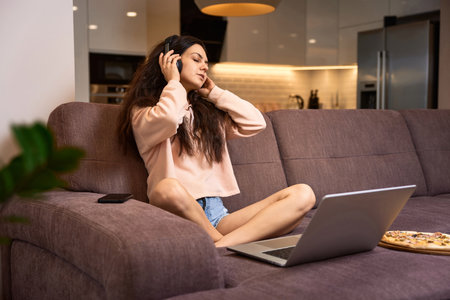 happy woman listening to music with headphones and using laptop on sofa at homeの写真素材
