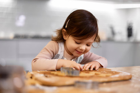 cute happy little child girl cutting gingerbread cookies with a cookie cutter in kitchen. festive gingerbread cookiesの写真素材