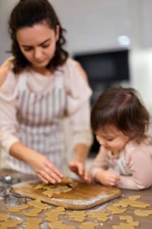 Happy family mother and little child daughter cutting cookies of raw gingerbread dough in kitchen....