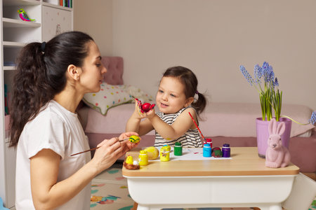 Happy mother and cute little child girl are preparing to celebrate Easter at home. Mom and daughter painting eggs before Easter together.の写真素材