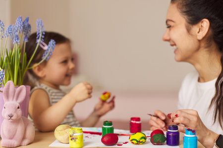Happy mother and little daughter are preparing to celebrate Easter at home. Mom and daughter painting eggs before Easter together. focus on eggsの写真素材