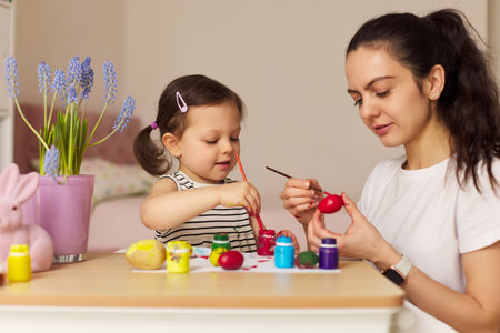 Happy mother and cute little child girl are preparing to celebrate Easter at home. Mom and daughter painting eggs before Easter together.の写真素材