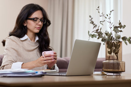 Beautiful woman in shirt using laptop while working at homeの写真素材