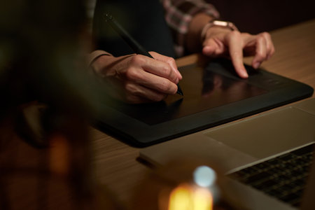 female hands with graphic tablet retouching photo on laptop computer at nightの写真素材