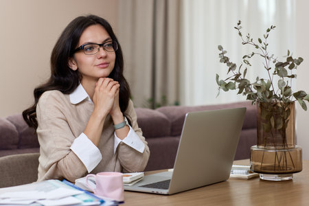 thinking woman in shirt using laptop while working at homeの写真素材