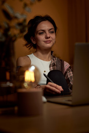 beautiful graphic designer woman working at home office remotely using digital graphic tablet and laptop in the eveningの写真素材