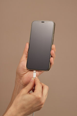 female hand plugging charger cord into smartphone to charge battery on beige background, Wired...