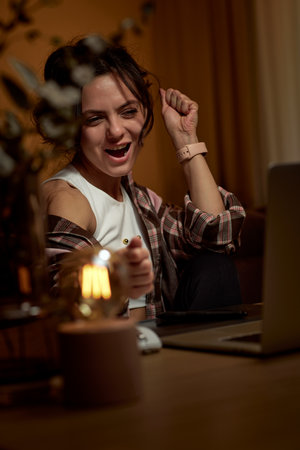 happy excited graphic designer woman with open mouth raised fist up working using digital graphic tablet at home in the eveningの写真素材