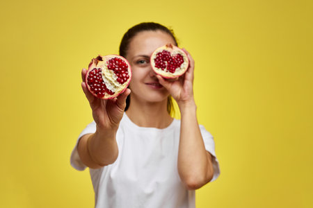 Beautiful happy woman holding pomegranate on yellow background, focus on pomegranateの写真素材