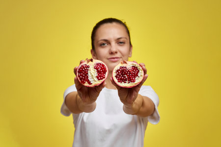 Beautiful happy woman holding pomegranate on yellow background, focus on pomegranateの写真素材