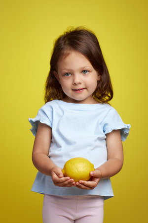 cute Caucasian little child girl holding lemon on yellow backgroundの写真素材