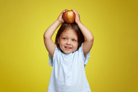 cute Caucasian little child girl holding apple on yellow backgroundの写真素材