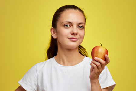 Portrait of happy woman holding apple isolated over yellow backgroundの写真素材