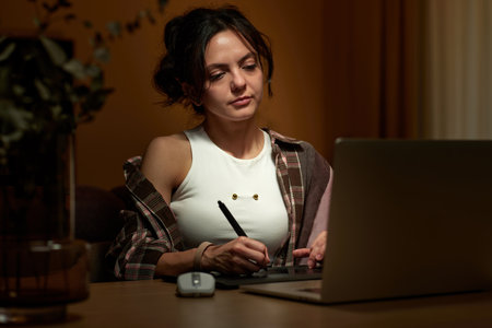 beautiful graphic designer woman working at home office remotely using digital graphic tablet with stylus and laptopの写真素材