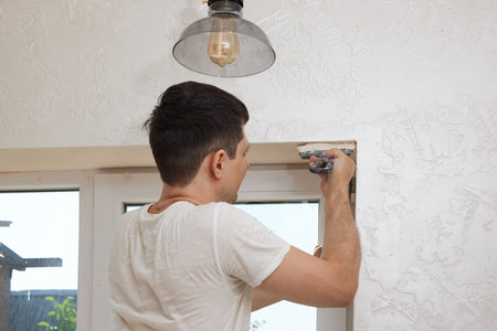 Caucasian plasterer man with a spatula applying finishing putty on a window openingの写真素材