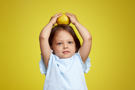 cute Caucasian little child girl holding lemon on yellow backgroundの写真素材