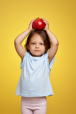cute little child girl holding a pomegranate on yellow background.の写真素材