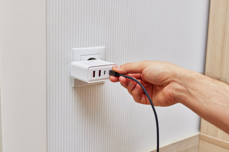 male hand insert a plug of the phone charger into socket at home