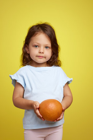 cute little child girl holding grapefruit on yellow backgroundの写真素材