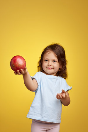 cute little child girl holding a pomegranate on yellow background.の写真素材