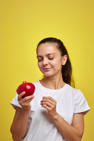 Beautiful happy woman holding pomegranate on yellow backgroundの写真素材