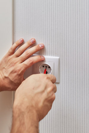 male hands installing electrical wall socket with a screwdriver at home