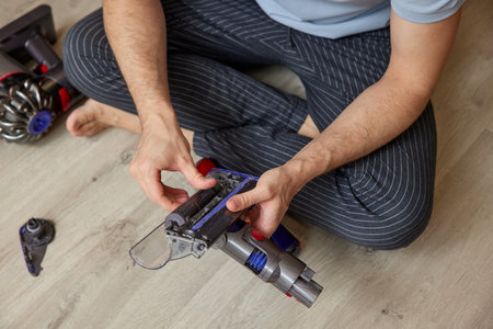 Man disassembling a cordless vacuum cleaner for maintenance in living room