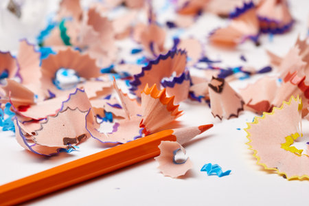 Orange pencil tip surrounded by colorful wood shavings on a white backgroundの写真素材