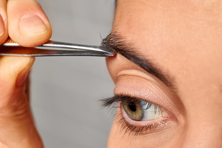 Woman grooming her eyebrow with tweezers, removing unwanted hair for precise shaping
