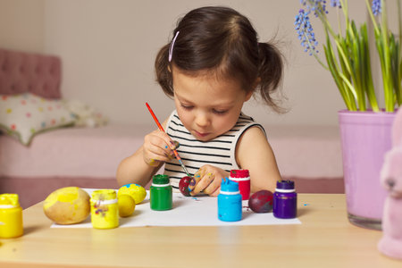 Little child girl paint Easter eggs at home. kid is preparing for Easter.