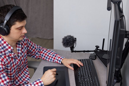 Man wearing headphones using a microphone and graphics tablet at his desk