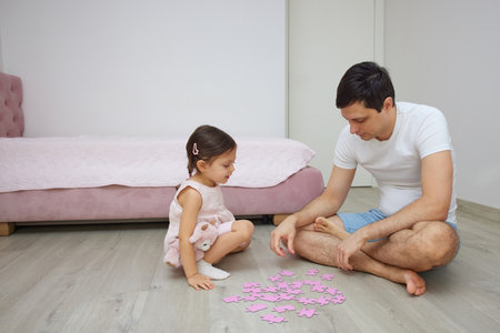 Father and daughter enjoying time together, bonding while solving a puzzle at homeの写真素材