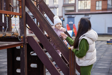 Mother smiling, encouraging young child climbing steps on outdoor playground