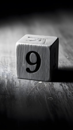 Black and white photo of wooden block with number nine on rough wooden surface in soft natural light.の素材
