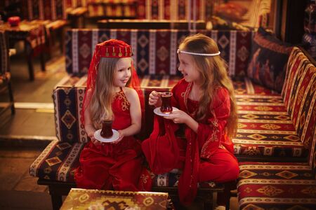 Two girls in folk Arabic costumes drinking Turkish tea together