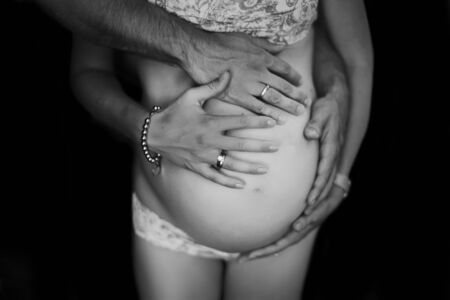 Pregnant couple's cuddles, black and white photo, faceless portrait.の写真素材