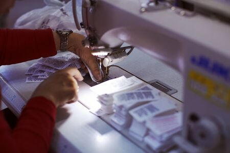 Worker on factory sewing on made in and brand name tags to produced cloths.