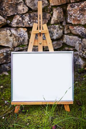 Easel staying om grass and moss near ancient stone walll with copy spaceの写真素材