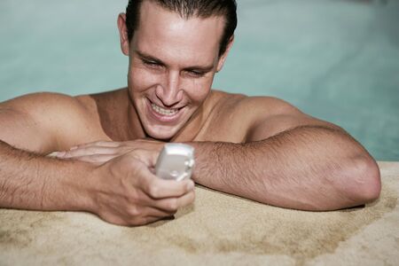 Male texting on mobile phone in swimming pool on holiday の写真素材