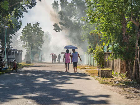 two ladies holding an umbrella walking on a dusty road on a sunny dayの写真素材
